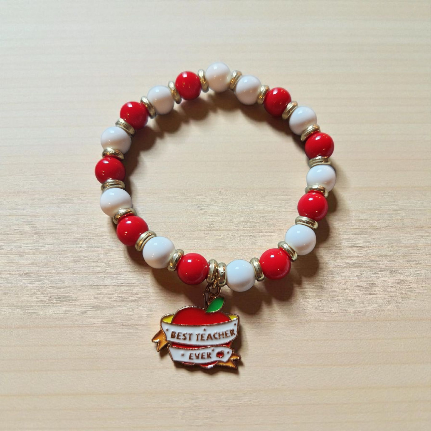Bracelet with red and white beads and a 'Best Teacher Ever' charm on a light wooden surface