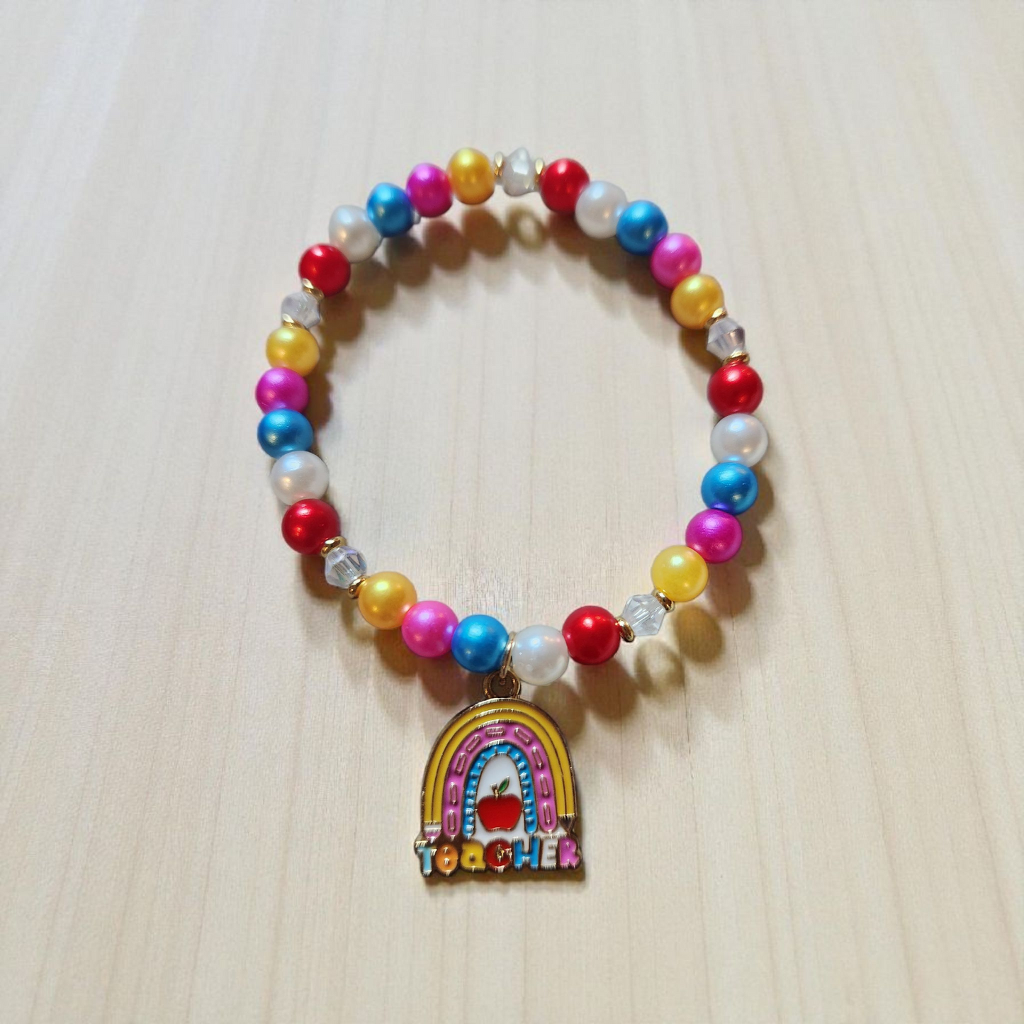 Colorful beaded bracelet with a rainbow charm and 'Teacher' text on a light wooden surface